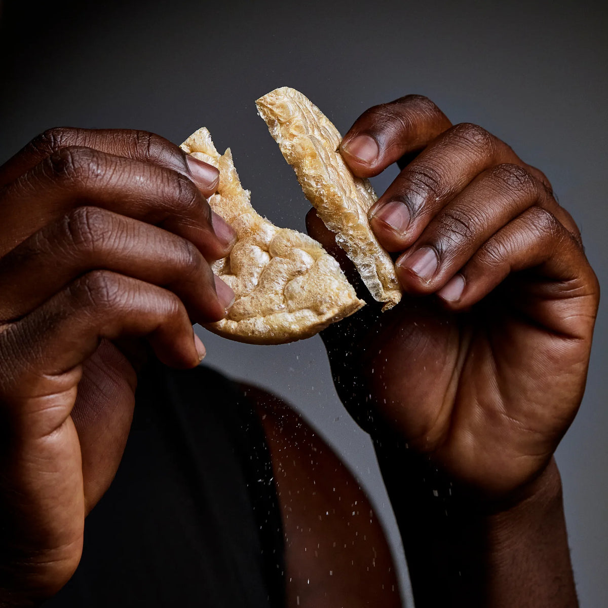 Hands snapping a Subtle Snacks Hint of Salt protein rice cake in half, crumbs falling
